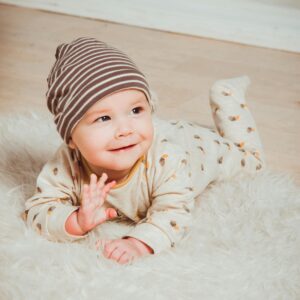 A cute baby in striped beanie lying on fluffy rug indoors, smiling with innocence.