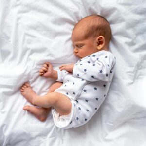 A serene image of a baby sleeping peacefully in a white onesie on a bed.