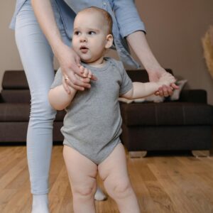 A mother gently helping her baby take first steps in a cozy home setting.
