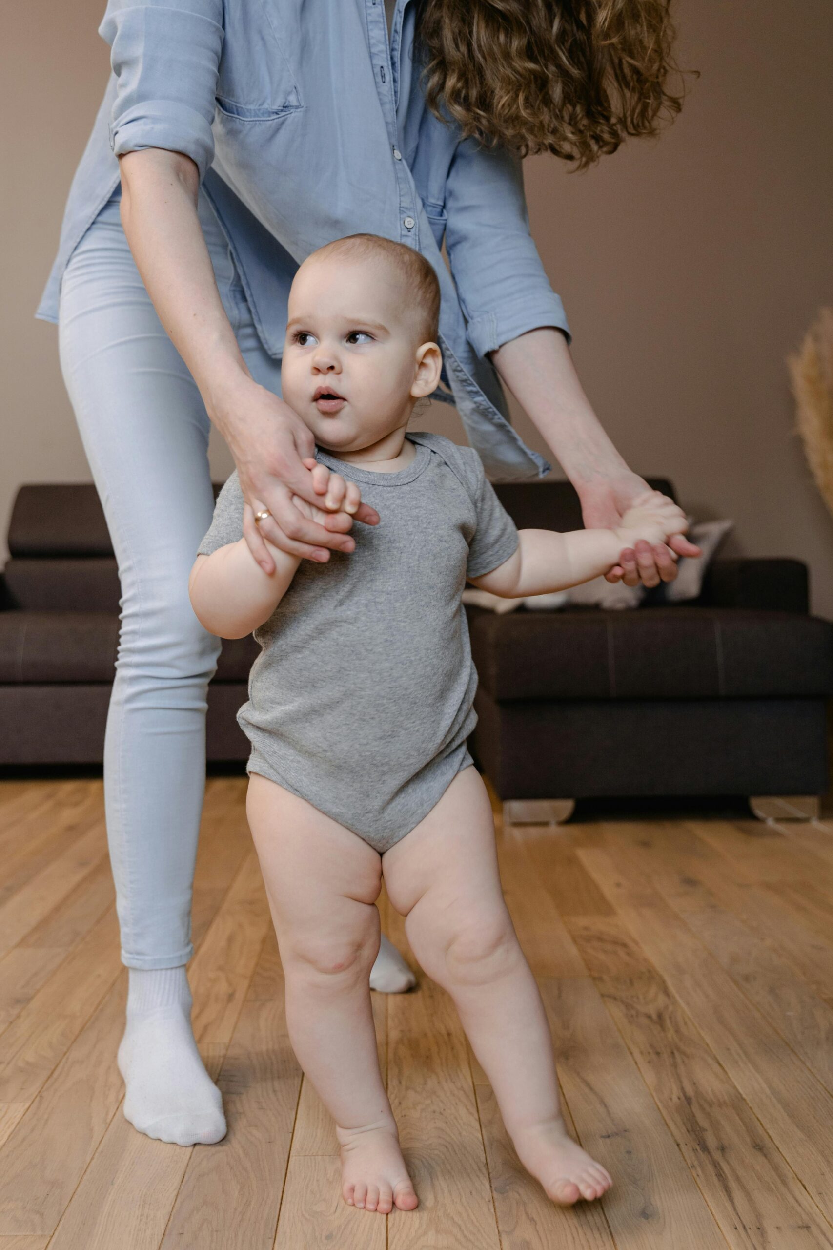 A mother gently helping her baby take first steps in a cozy home setting.