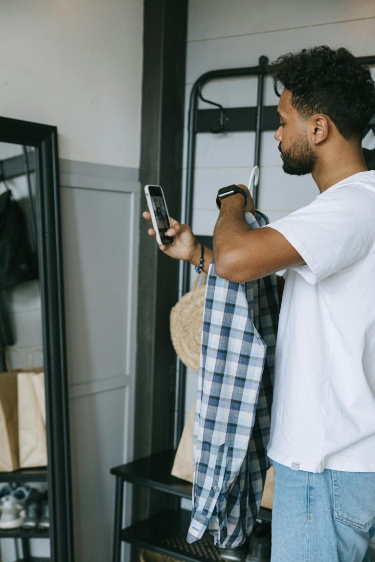 Young man holding a plaid shirt and using smartphone for online shopping. Casual indoor setting.